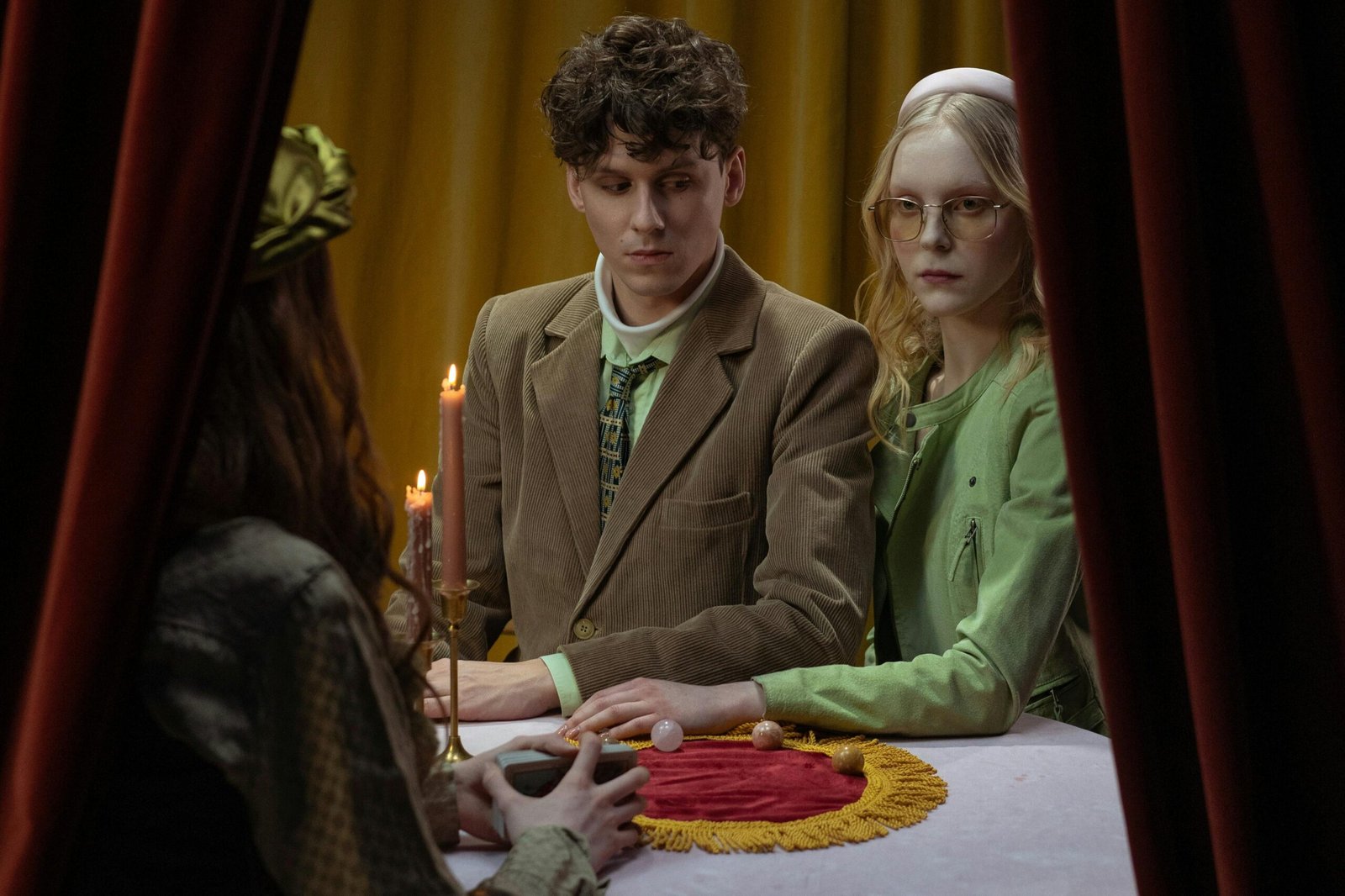 Young couple visiting a fortune teller in a mysterious setting with candles and draped curtains.